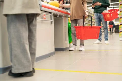Low section of several customers with plastic shopping baskets standing in queue Stock Photos