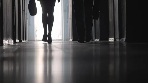 Low Section of Silhouettes of Colleagues Walking through Hallway Видео 100789324