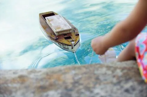 Low section view of a girl sitting at edge of swimming pool with toy boat in Stock Photos