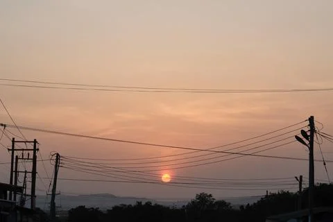 Low setting full round sun at sunset framed by electricity and t Stock Photos