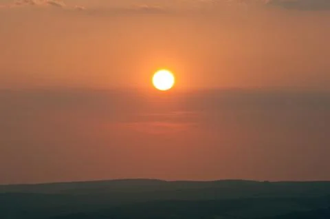Low setting sun over distant landscape Stock Photos