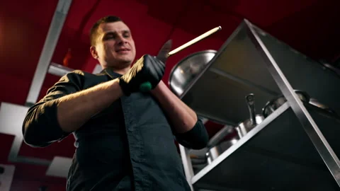 Low shot the chef stands in the kitchen in black jacket and sharpens his knives Stock Footage 273184231