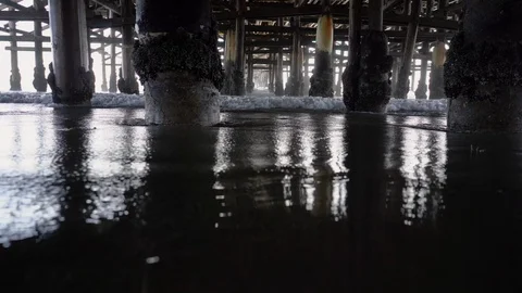 Low Shot Track Right of Waves Rolling in and Out Under Old Weathered Pier Stock Footage 96043756