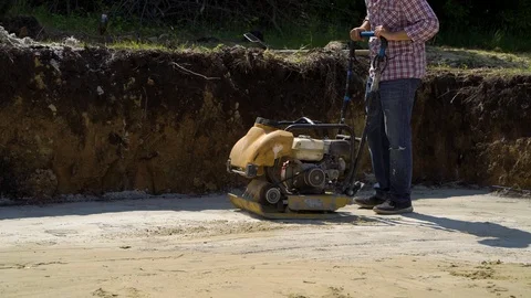 Low shot of worker using vibrating rammer on sand surface Stock Footage 107985758