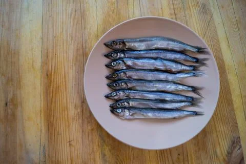 Low side view of small silver fish in a beige plate on a wooden table, close 写真素材