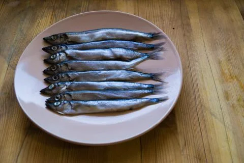 Low side view of small silver fish in a beige plate on a wooden table, close 写真素材