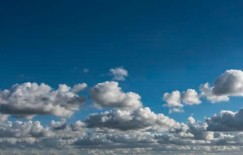 Low small compact and vivid white clouds against a blue gradient sky backgrou Stock Photos