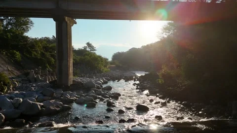 Low Sun Beneath a Road Bridge Over a Rocky River Vídeo Stock 347499877
