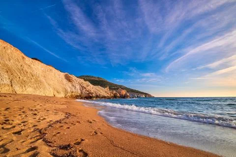 Low sun over beach, cliffs and hills and deep azure sea. Agios Ioannis beach Stock Photos