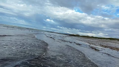 Low tide beach with seaweed and waves under dramatic cloudy sky Vidéo 332680115