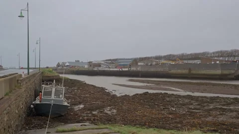 Low Tide View Down River to the Sea with Fishing Boat Grounded by Harbour Wall Stock Footage 332069639