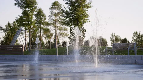 Low view of splash pad water jets spraying at sunset when park is empty Video stock 233948060