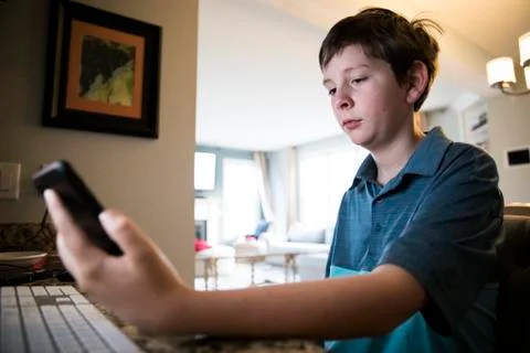 Low View of Tween Boy at Computer Desk Reading Texts on iPhone Stock Photos