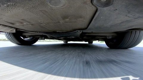 Low view under the car of the car wheels turning while driving Stock Footage