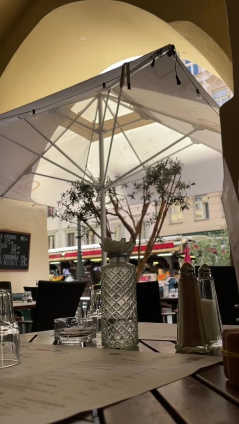 Low viewpoint cafe table with condiments under market umbrella and arched Vídeos de archivo 344585051