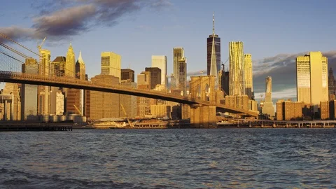 Low wide angle of Manhattan skyline lit by rising sun and reflecting East River Stock Footage 99096344
