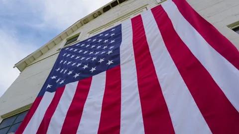 Low wide wrap around view of huge American flag draped on rustic barn Vidéo 202152088