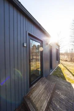 Low winter sun on dark vertical clad tiny house with lens flare Stock Photos