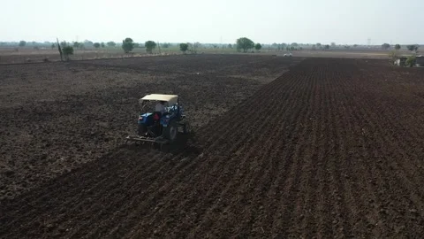 Lower angle mid air perspective following a blue agricultural vehicle pulling a Stock Footage 337199088