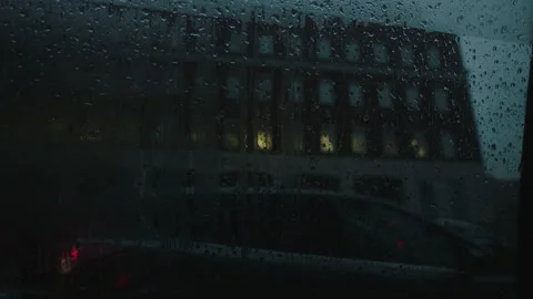 Lower angle rainy car window pov parked car and brick building in the distance Stock Footage 251221638