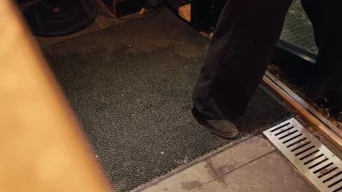 Lower legs stepping on threshold mat at doorway, dark trousers and boots on wet Stock Footage 330026904