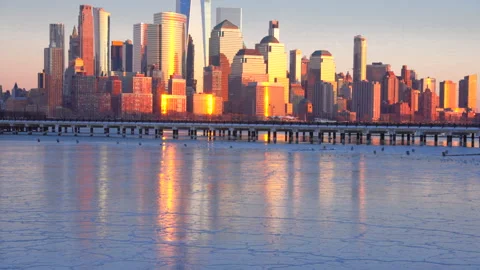Lower Manhattan skyscraper stands beyond frozen Hudson River in dusk. Vídeo Stock 336643723