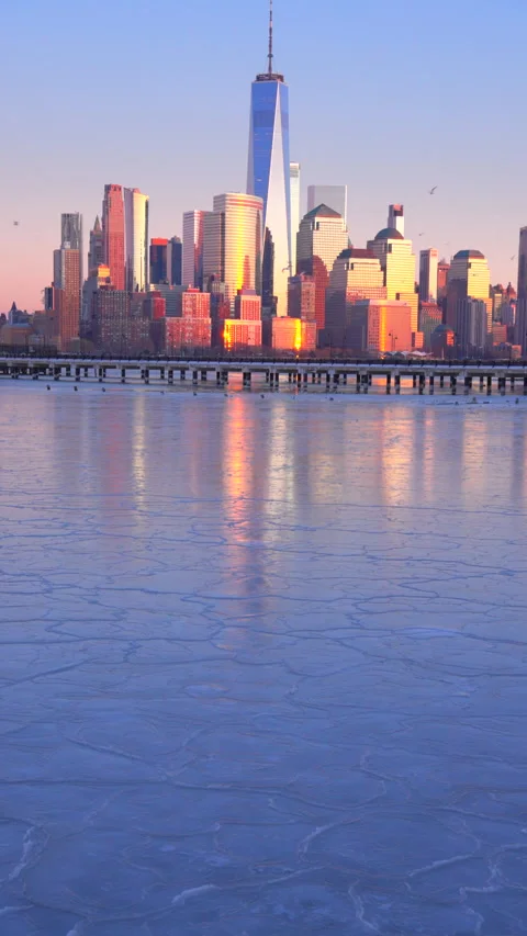 Lower Manhattan skyscraper stands beyond frozen Hudson River in dusk. Vídeo Stock 336644409