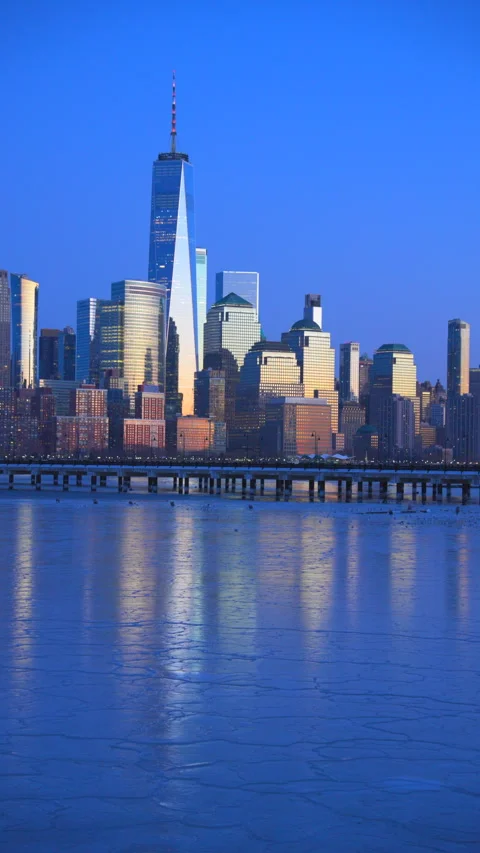 Lower Manhattan skyscraper stands beyond frozen Hudson River in dusk. 库存影片 336649661