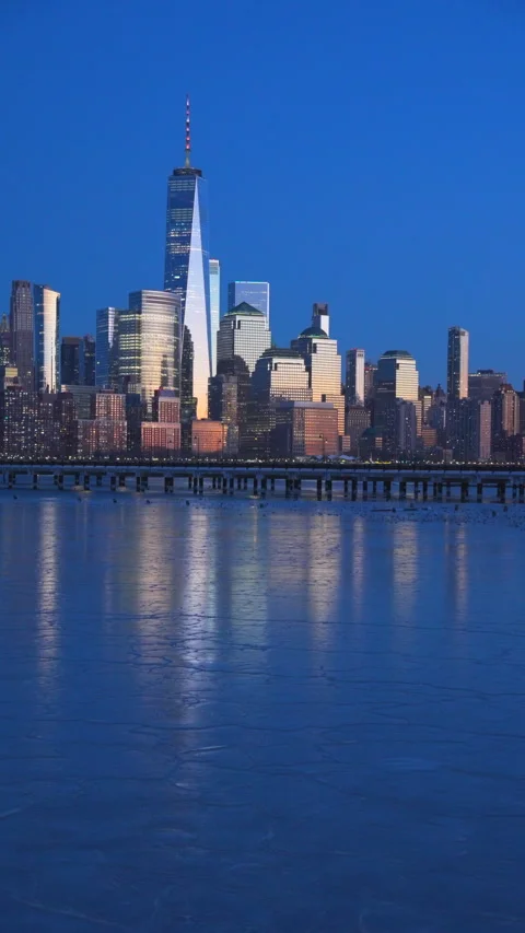 Lower Manhattan skyscraper stands beyond frozen Hudson River in dusk. Vídeo Stock 336650690