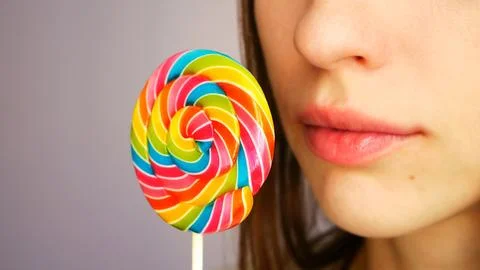 A lower part of the face of young lady holding a beautiful multicolored lollipop Stock Photos