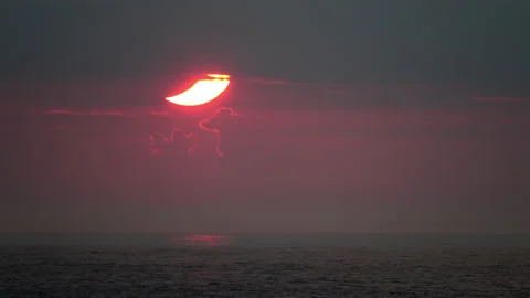 Lower portion of crescent-shaped partial solar eclipse rises into a cloud Stock Footage 155669929