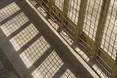 Lower portion of iron gate sealed with net and its shadow on ground Stock Photos