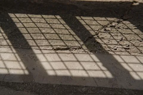 Lower portion of iron gate sealed with net and its shadow on ground Stock Photos