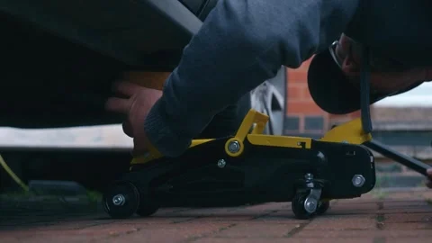 Lowering car with hydraulic floor jack while adjusting wooden support block Stock Footage 340195377