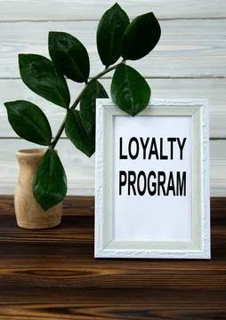 LOYALTY PROGRAM - words in a white frame on a brown wooden table with a vas.. Stock Photos