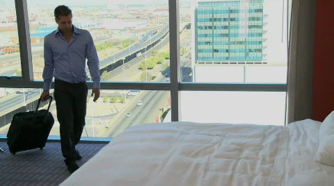 LS PAN OF A BUSINESSMAN WALKING INTO HIS HOTEL ROOM AND LYING ON THE BED Stock Footage
