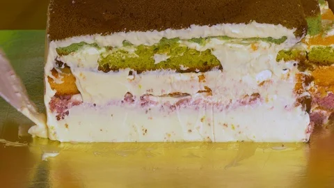 Lubricate the biscuit cake with multi-colored cake layers with butter cream Stock Footage 108557845
