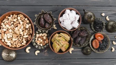 Lukum dates dried fruits baklava nuts earthen metallic bowl wooden desk Stock Photos