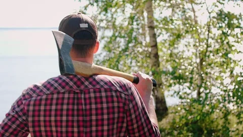 Lumberjack with a large axe on his shoulder goes to the shore of the lake, river 動画素材 148131914