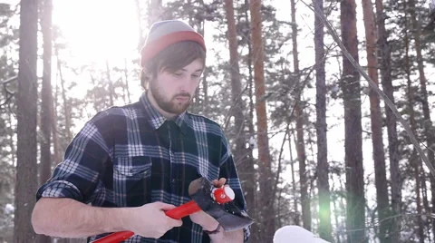 Lumberjack stands and sharpens his ax in the woods, light leakage surround him Stock Footage 60050100