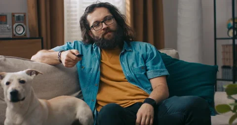 Lumberjack-type guy sits on living room couch firing up music from speakers with 스톡 동영상 218181036