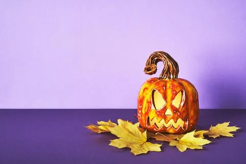 Luminous Ceramic Pumpkin jack lantern with yellow autumn leaf on purple backg 写真素材