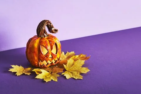 Luminous Ceramic Pumpkin jack lantern with yellow autumn leaf on purple backg Stock Photos