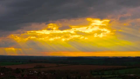 Luminous cloud formation opening with powerful sunbeams over rolling countryside Stock Footage 336546143