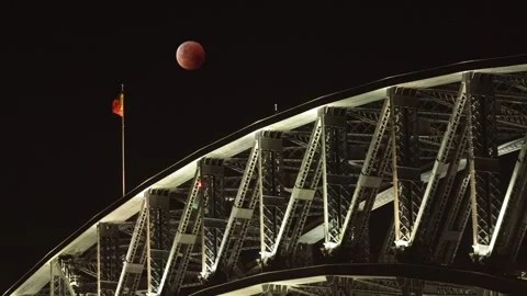 Lunar eclipse blood red moon over Sydney Harbour Bridge with flags Stock Footage 254746680