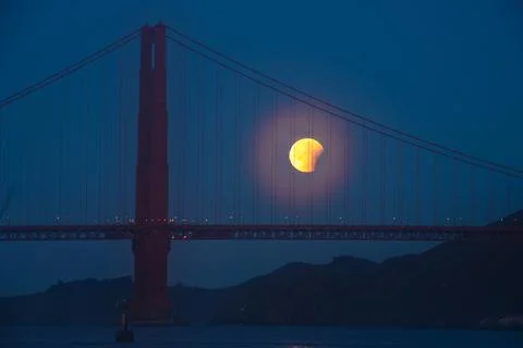 Lunar eclipse over the Golden Gate Bridge at night with a glowing moon Stock Photos