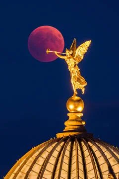 Lunar eclipse, the red moon behind the golden statue of an angel blowing i... Stock Photos