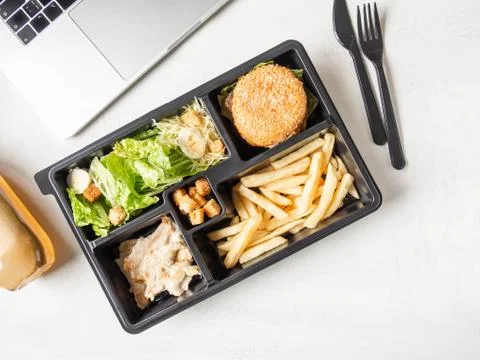 Lunch box in black plastic package for take away or food delivery and laptop Stock Photos