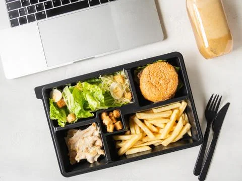 Lunch box in black plastic package for take away or food delivery and laptop Stock Photos