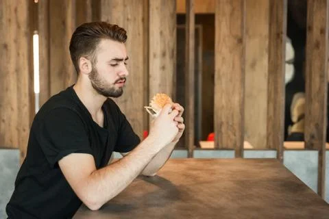 Lunch at the cafe. A young guy looks at the burger and wants to sit down. Stock Photos